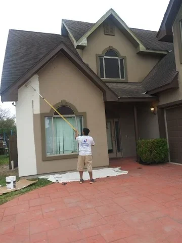 Painter applying exterior paint to stucco house facade with brick patio
