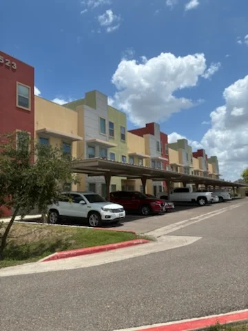Multi-unit residential building with red, yellow, and tan exterior paint and covered parking area