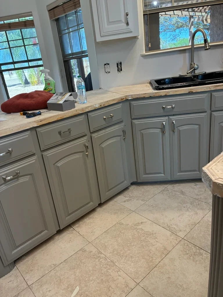 Gray painted kitchen cabinets with chrome hardware, light wood countertops, and white walls