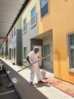 Painter applying exterior paint to house facade with yellow and gray color scheme