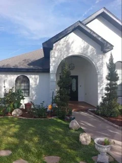 White stucco house exterior with dark trim, arched entry, and landscaping