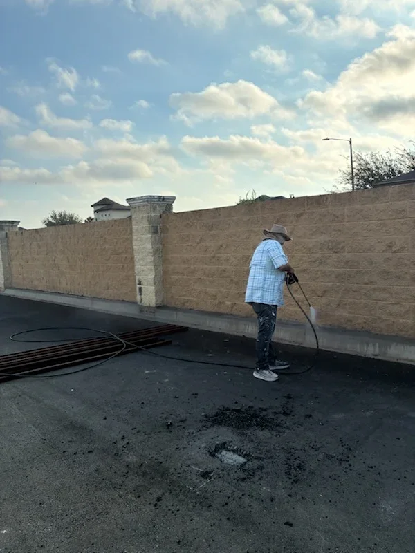 Worker pressure washing flat concrete roof with brick parapet wall in background
