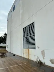 White painted commercial building exterior with metal siding and louvered vent