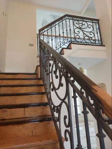 White painted stairwell walls with wooden stairs and ornamental black iron railing