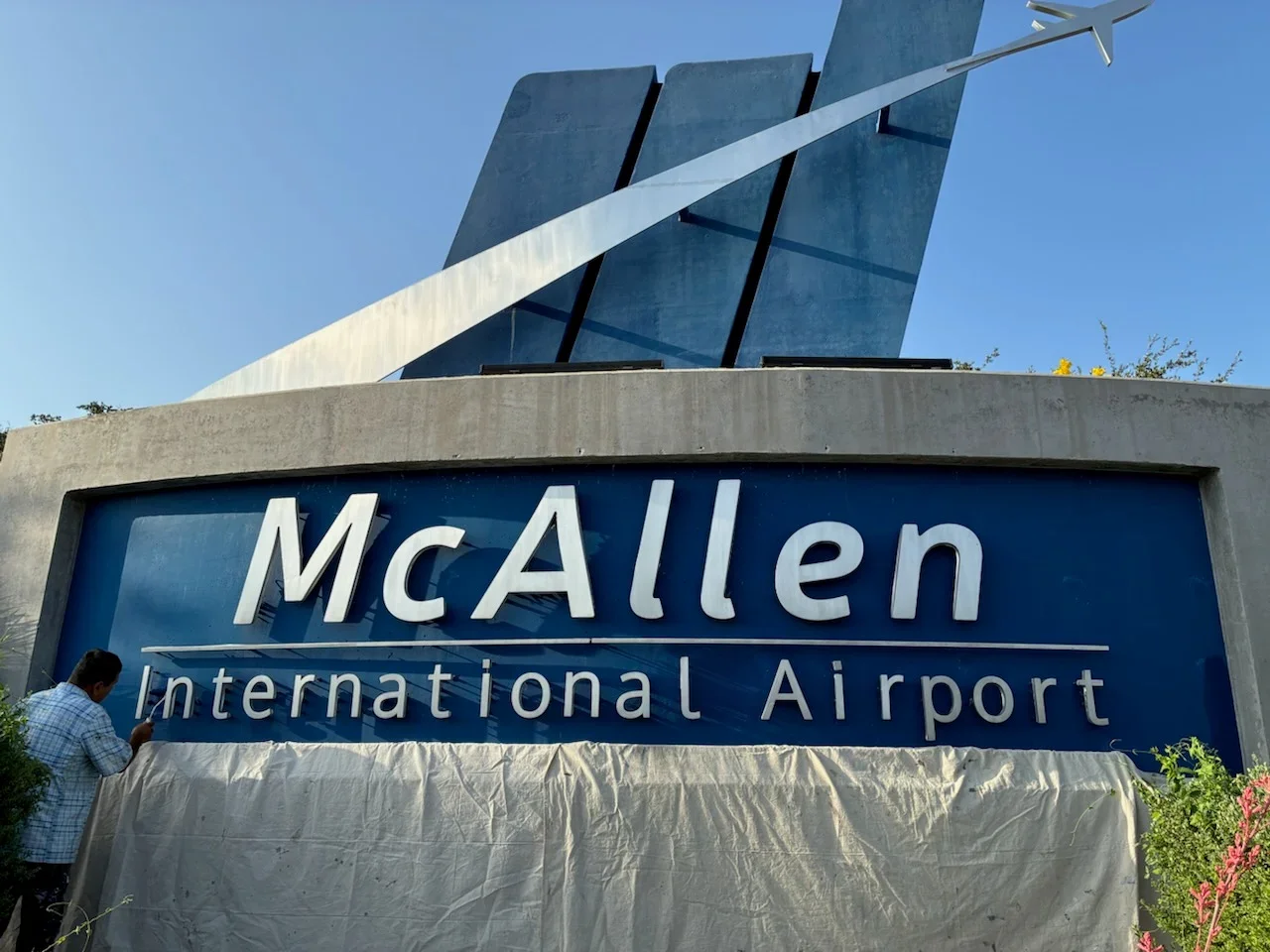 Blue and white airport sign with painted lettering on concrete base and metal framework