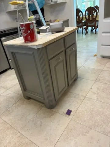 Gray-painted kitchen island with detailed trim and travertine countertop in open kitchen space