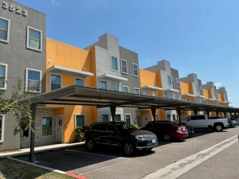 Multi-story residential building with yellow and gray exterior paint, carport, and parked vehicles