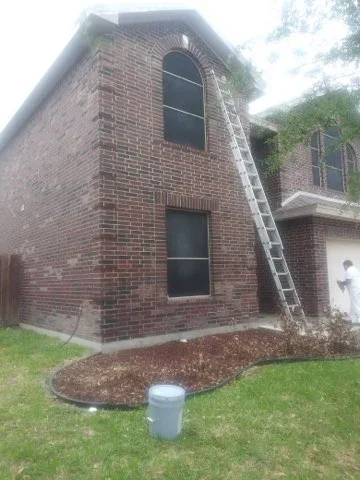 Two-story brick home exterior with fresh paint application and professional ladder setup
