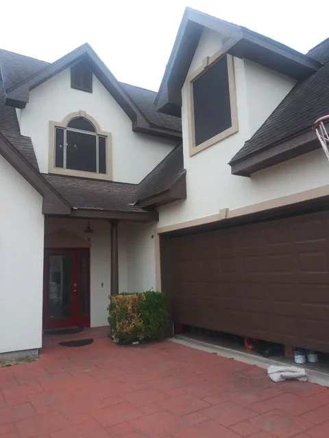 White stucco two-story house with dark brown trim, painted gables, and brown garage door