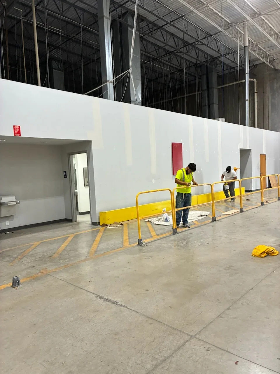White drywall walls with red and tan accents, yellow safety floor lines, industrial warehouse interior