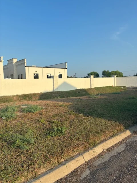 Cream-painted residential building with matching perimeter fence and prepared landscaping