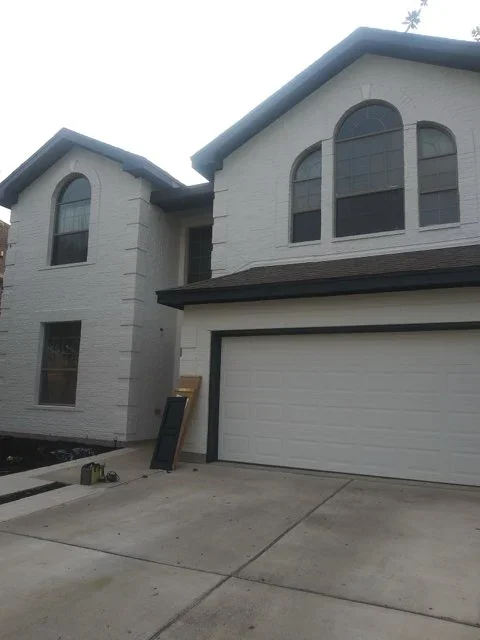 White brick two-story home with dark trim and arched windows, freshly painted exterior