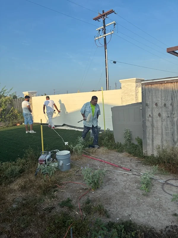 Exterior wall painting in progress on residential concrete block structure with yellow paint finish